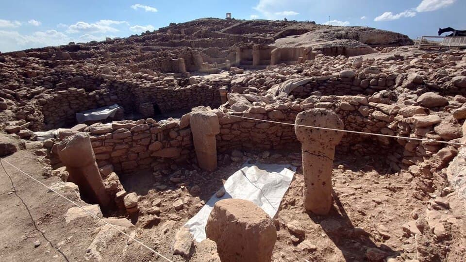 Aerial view of the Karahantepe archaeological site in Şanlıurfa, Turkey, showing excavated stone structures carved into limestone bedrock on a hillside