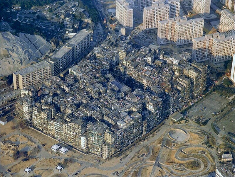 A wider 1989 aerial view of Kowloon Walled City from a slightly different angle, showing the monolithic building block surrounded by streets.